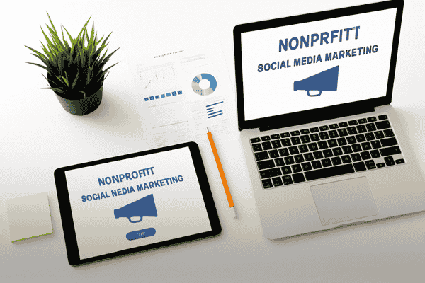 A modern workspace featuring a laptop and tablet displaying nonprofit social media marketing titles next to analytical planning documents.