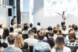 A diverse audience of nonprofit professionals attending a marketing conference session in 2026, listening to a speaker present on stage.